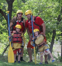 Two adults and two children posing with paddles and helmets on the riverbank Raft Masters Colorado